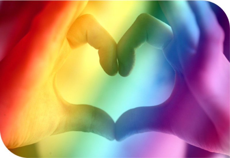 Das Bild zeigt zwei Hände, die vor einem Regenbogenhintergrund ein Herz formen.
