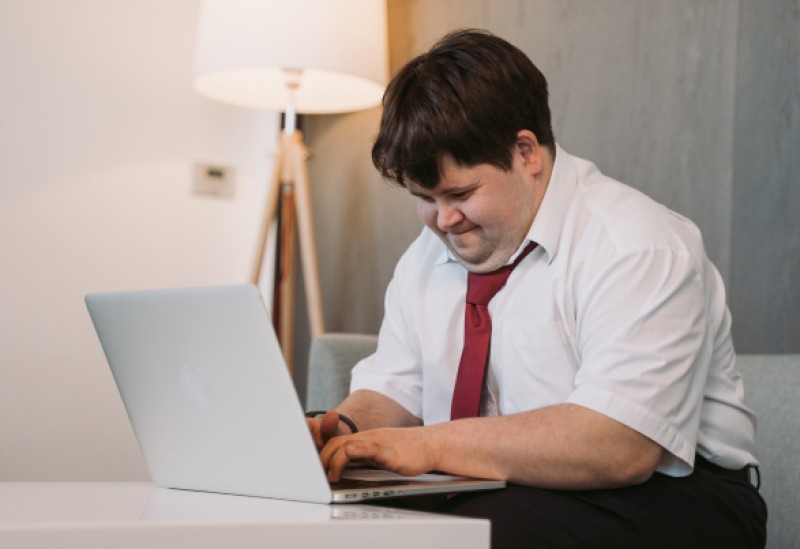Das Bild zeigt eine Person mit Down-Syndrom, die an einem Laptop arbeitet. Es verdeutlicht die universelle Fähigkeit und Inklusivität am Arbeitsplatz.