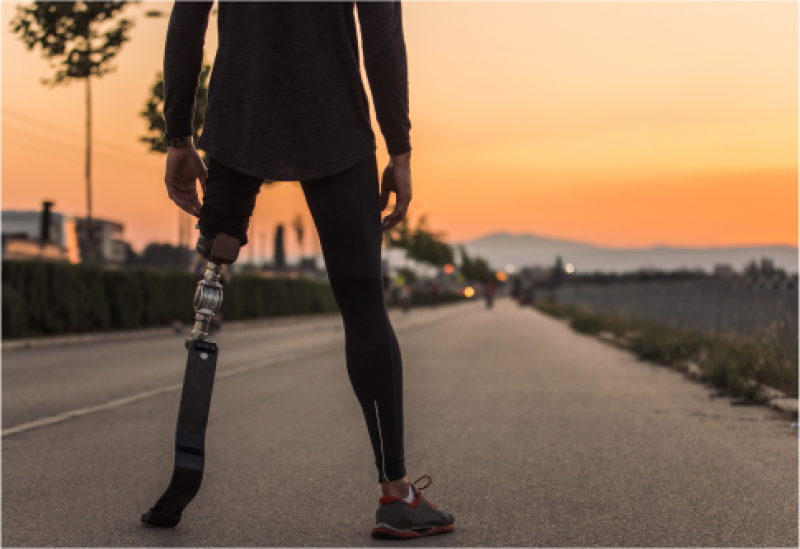 Das Bild zeigt eine Person mit einer Beinprothese bei Sonnenuntergang auf einer Straße.